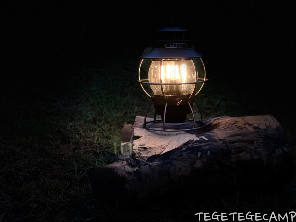 暗所で屋外撮影したベアボーンズレイルロードランタンと薪